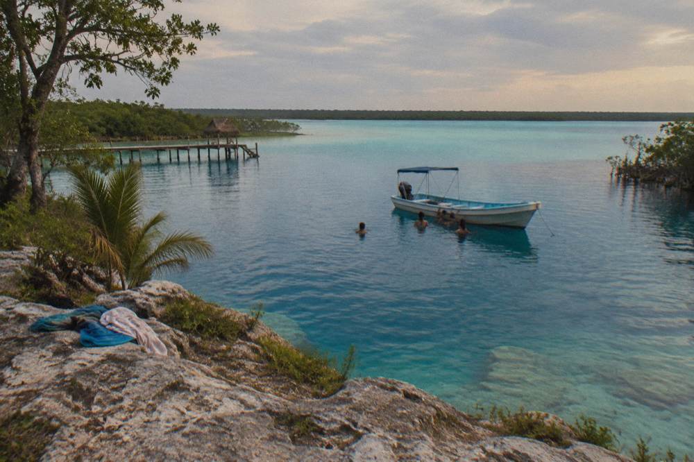 Swimmers in clear turquoise water near a boat anchored on Bacalar Lagoon