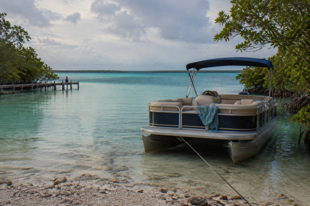 A pontoon boat moored in shallow turquoise water beside mangroves on Bacalar Lagoon